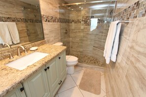 Et moderne badeværelse med en brusekabine i glas, en bordplade i granit, et toilet og et stort spejl.