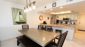 A modern kitchen with a central island, a dining area with a large table and chairs, and a clock on the wall. - Shore to Please - Condo 402: A cozy oceanfront  2-bedroom retreat in South Padre Island. (South Padre Island)