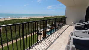 A balcony with a view of the beach, a pool, and outdoor seating. - Shore to Please - Condo 402: A cozy oceanfront  2-bedroom retreat in South Padre Island. (South Padre Island)