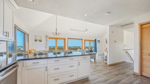A modern kitchen with a large island, white cabinetry, and a view of the ocean.