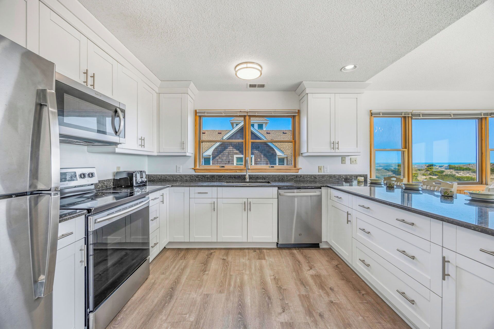 A modern kitchen with white cabinetry, stainless steel appliances, and a large window offering a view of a house and landscape.