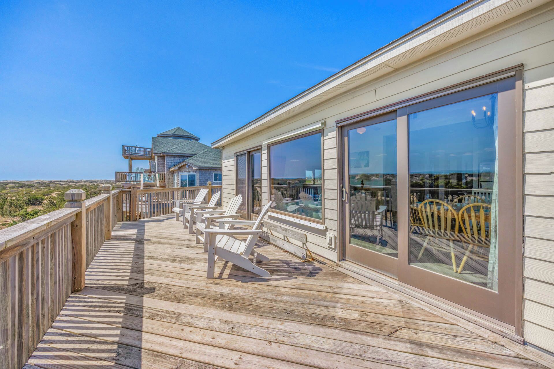 Une terrasse en bois avec des chaises et un balcon vitré donnant sur la plage.