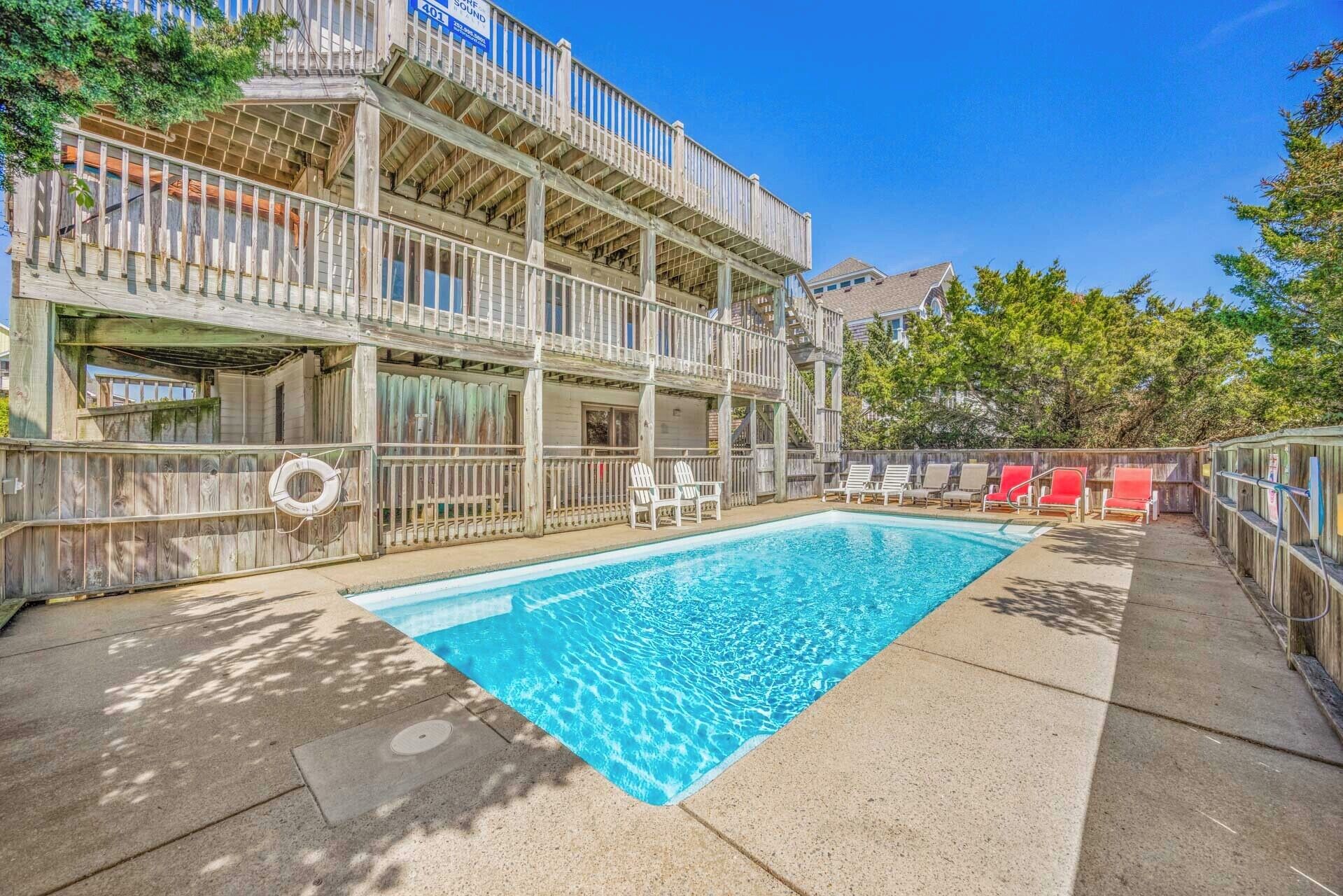 A swimming pool with a wooden deck and lounge chairs, surrounded by a wooden fence and trees.