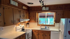 A kitchen with wooden cabinets, a stove, a sink, and a window with a view of trees. - Relax and enjoy this private location in Hampton Bays (Hampton Bays)