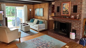 A cozy living room with a fireplace, wooden walls, and a comfortable seating area. - Relax and enjoy this private location in Hampton Bays (Hampton Bays)