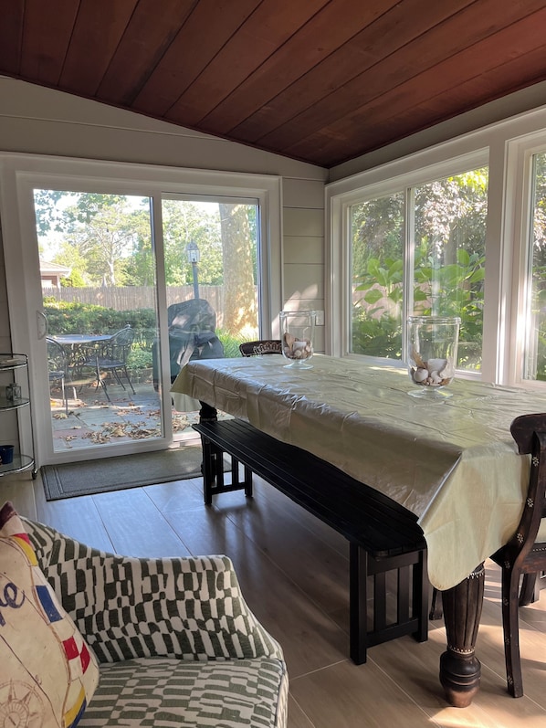 A dining area with a table covered by a white tablecloth, a bench, and a chair. There is a glass vase with flowers on the table.