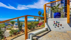 A staircase leading to a balcony with a view of the ocean and palm trees.