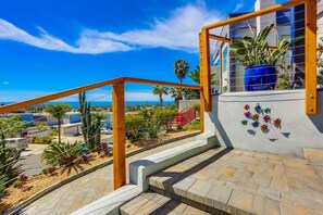 Un escalier menant à un balcon d’où l’on peut admirer l’océan et les palmiers.