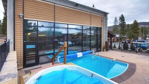 Une piscine située à côté d’un bâtiment doté de grandes fenêtres et d’une façade en bois.