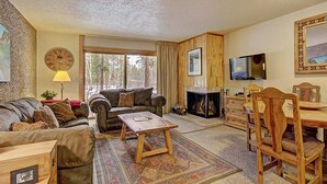 Un salon chaleureux avec une cheminée, un canapé, une table basse et un coin repas comprenant des chaises et une table en bois.