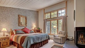 Une chambre à coucher avec un grand lit, une chaise, une cheminée et une fenêtre avec des rideaux.