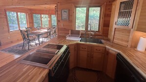 Ein Holzblockhaus im Inneren mit einer Küchenzeile, die einen Herd, ein Spülbecken und einen Esstisch mit Stühlen zeigt.