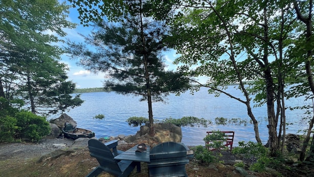 Ein Campingplatz am Seeufer mit Tisch und Stühlen, umgeben von Bäumen und Felsen.