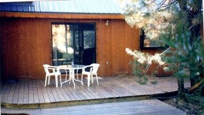 Een houten terras met een tafel, stoelen, een deur en een kleine boom.