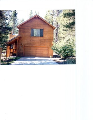A wooden cabin with a garage, surrounded by trees.