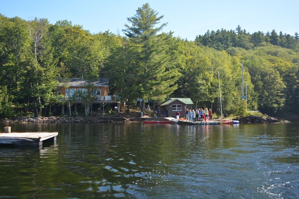 The view of the cottage and boathouse from the lake, and the family on the dock