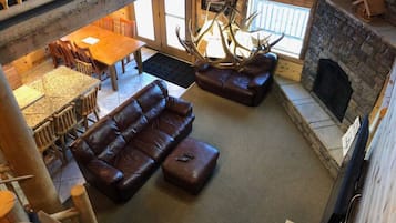 A cozy living room with a stone fireplace, leather sofa, and a large antler chandelier.