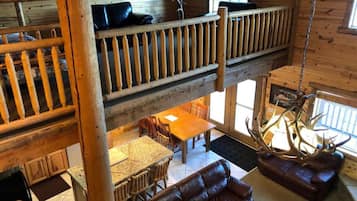 A multi-level wooden cabin with a dining area, leather seating, and a hanging antler sculpture.