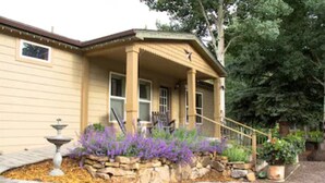 Ein Haus mit überdachter Veranda, Steinstufen und einem Garten mit violetten Blumen.