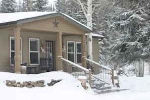 A snow-covered building with a porch, a star on the roof, and a wooden fence.