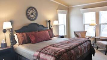 A bedroom with a large bed, two bedside tables with lamps, a clock on the wall, and a window with a view.