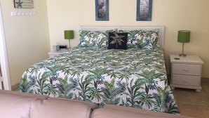 Un dormitorio con una cama, dos mesitas de noche, una lámpara verde, un cojín y un adorno en la pared.