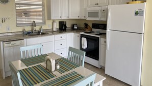 Cocina compacta con armarios blancos, microondas, refrigerador y un comedor con mesa y sillas.