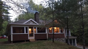 Une cabane avec une cheminée en pierre, une véranda et un petit garage attenant.