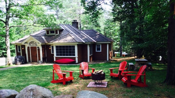 Une maison avec un porche, des fauteuils Adirondack rouges, un foyer extérieur et une cheminée en pierre.