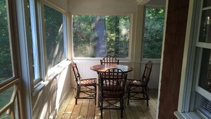 Une véranda avec une table et des chaises en bois, de grandes fenêtres et une vue sur les arbres.