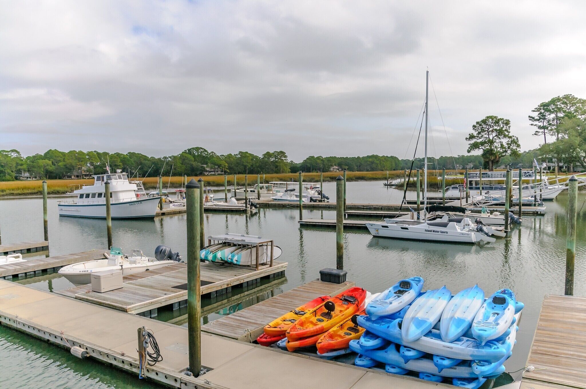 A marina with boats docked, kayaks on the dock, and a calm water body.