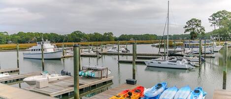 A marina with boats docked, kayaks on the dock, and a calm water body.