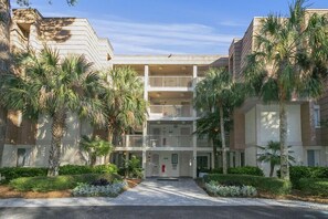 Un hotel de varios pisos con un patio central, palmeras y cielo despejado.