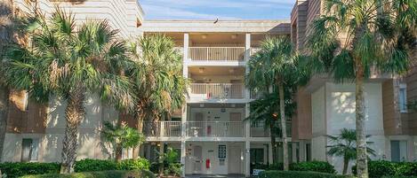 A multi-story hotel with a central courtyard, palm trees, and a clear sky.