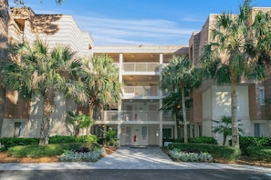 A multi-story hotel with a central courtyard, palm trees, and a clear sky. - Stunning Condo in Plantation Club with Views of the Golf Course and On-site Amenities! (Hilton Head)