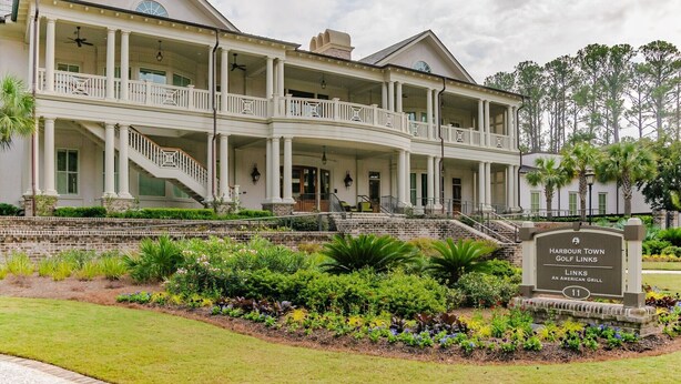 Un grande edificio a più piani con un portico coperto, un cartello che indica Harbour Town Golf Links e un giardino curato sul davanti.