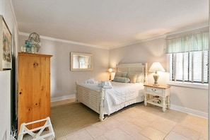 A bedroom with a bed, bedside tables, a dresser, a mirror, and a window with shutters. - Stunning Condo in Plantation Club with Views of the Golf Course and On-site Amenities! (Hilton Head)