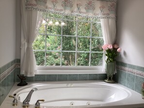 Um banheiro com banheira, janela com cortinas florais e um vaso com flores.