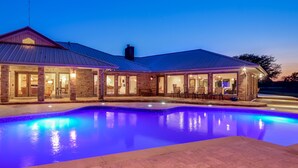 Una casa grande con piscina, muros de piedra y techo de metal.