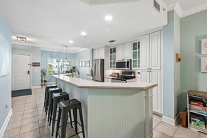 A modern kitchen with a central island, stainless steel appliances, and a bar stool seating area. - Beautiful 2nd Floor Villa Near Coligny Plaza (Hilton Head Island)