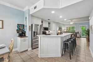 A modern kitchen with white cabinetry, stainless steel appliances, and a central island with bar stools.