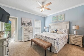 Ein Schlafzimmer mit einem Bett, einem Nachttisch, einer Kommode, einem Deckenventilator und Kunstwerken an den Wänden.