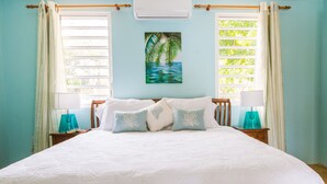Ein Schlafzimmer mit einem großen Bett, zwei Nachttischen, einer Wand-Klimaanlage und einem Fenster mit Vorhängen.