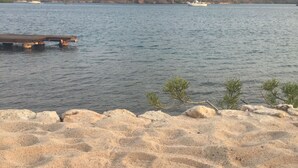 Ein Sandstrand mit Blick auf eine felsige Insel und ein Boot in der Ferne.