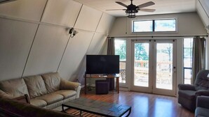 Una sala de estar con ventilador de techo, televisor sobre un mueble bajo, sofá y mesa de centro.