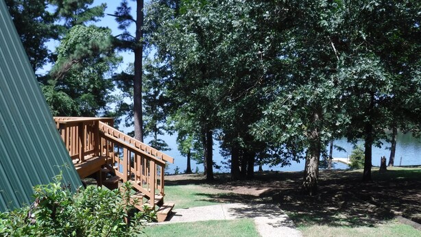 Una terraza de madera con una escalera que lleva a una cabaña junto a un lago, rodeada de árboles.