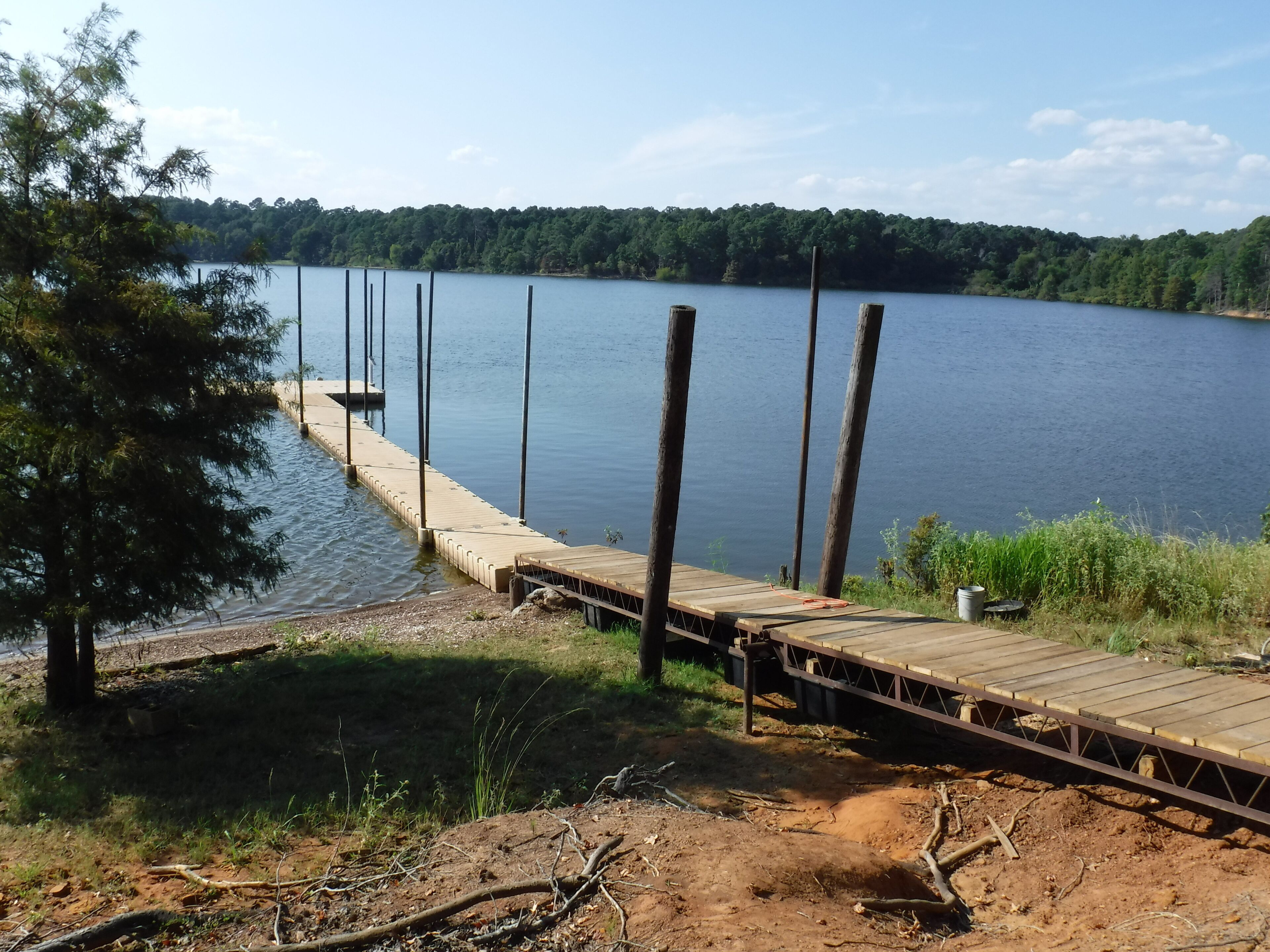 Un muelle de madera que se adentra en un lago tranquilo, rodeado de árboles y un cielo despejado.