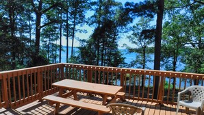 Una terraza de madera con una mesa y sillas de picnic, con vista a un lago rodeado de árboles.