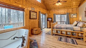 Una baita con interni in legno, un'ampia finestra, un letto, una panca di legno e una vasca da bagno.