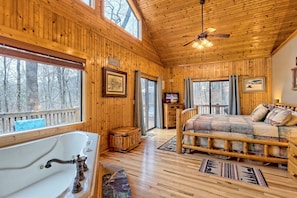 A cabin with a wooden interior, a large window, a bed, a wooden bench, and a bathtub.